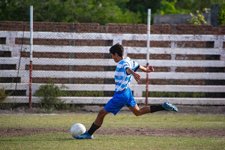 A boy kicks a soccer ball on an outdoor grassy field during the day.