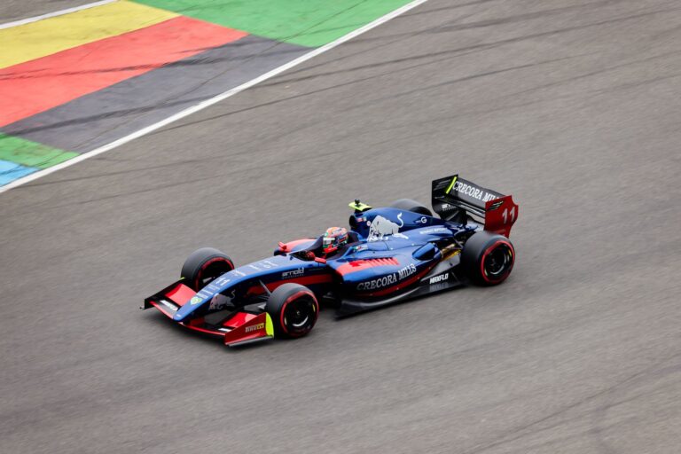Blue race car speeding on a track with colorful markings, showcasing motorsport action.