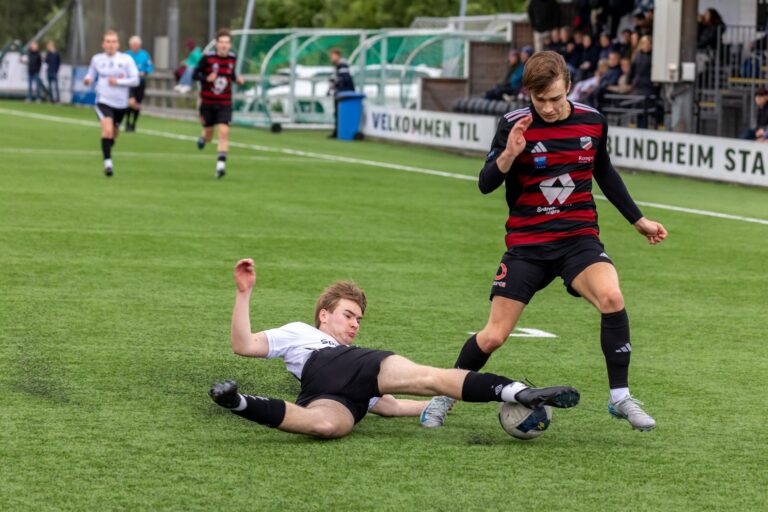 Intense football match showing a sliding tackle in action at Blindheim Stadium, Norway.