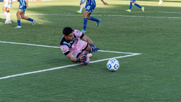 Goalkeeper makes a save on a sunny day during an intense soccer match.