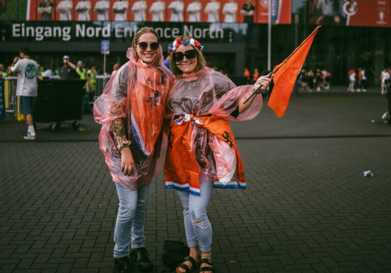 Two joyful soccer fans in raincoats and flags at a stadium entrance, enjoying a vibrant event.