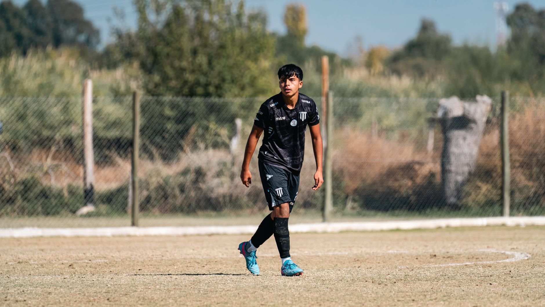 A young soccer player in black uniform focused during a game on an outdoor field.