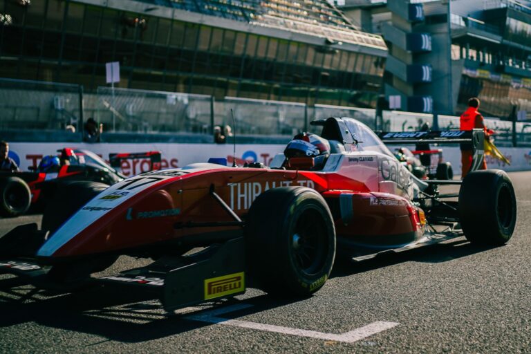 Close-up of a red Formula racing car on a track during a daytime event with spectators in the background.