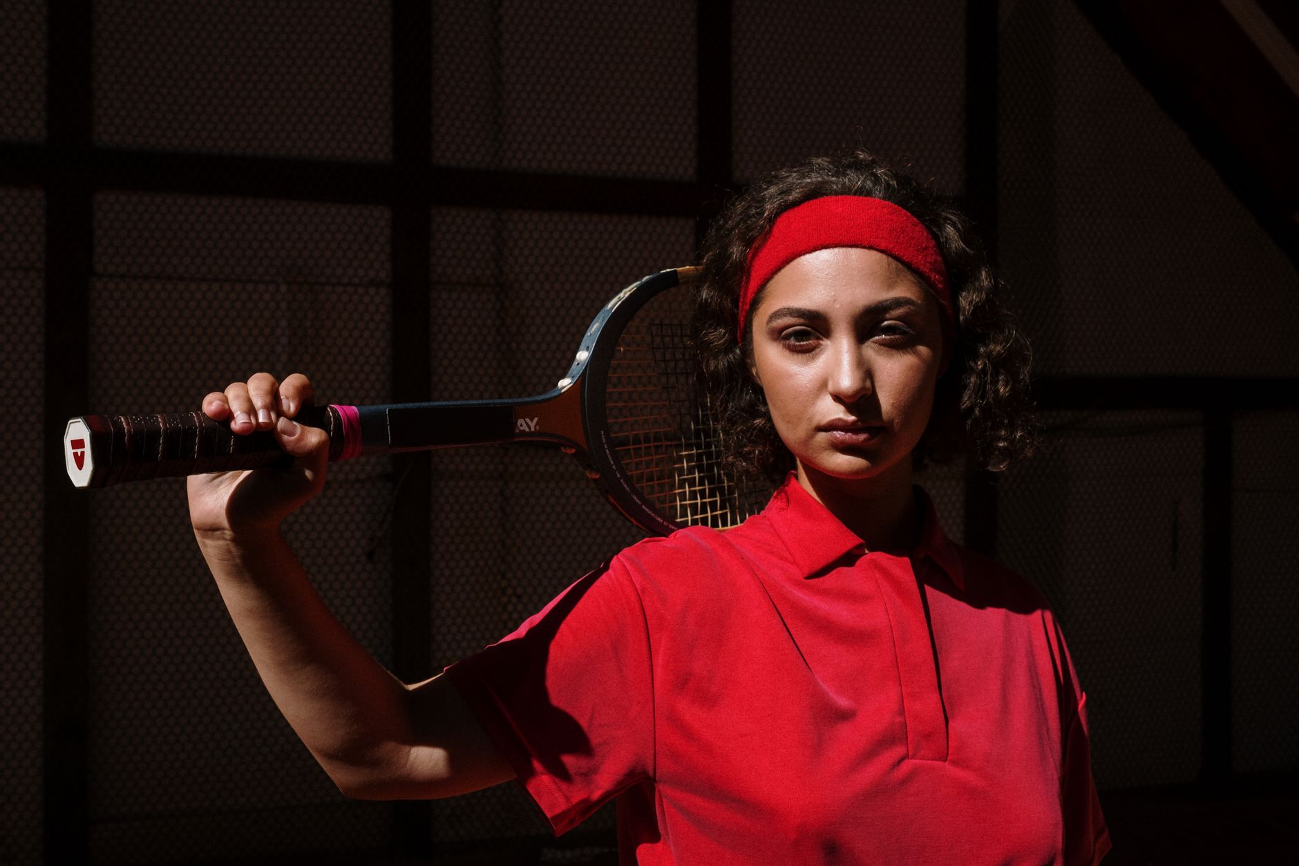 Portrait of a serious female tennis player holding a racket indoors.