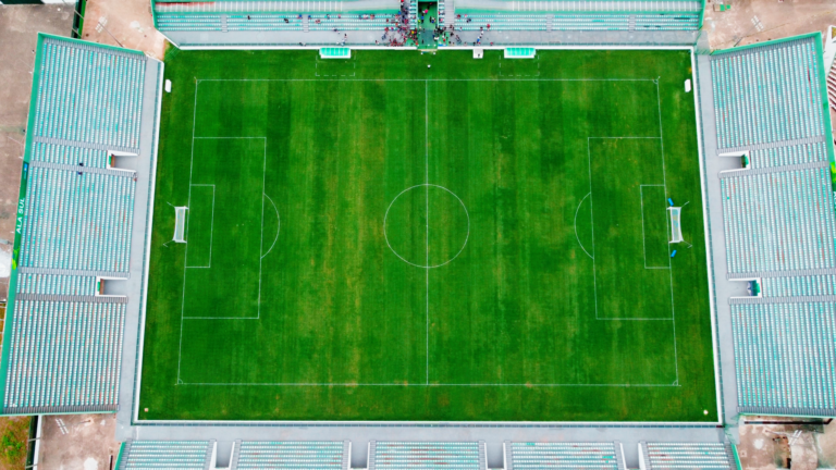 Drone shot of an empty soccer stadium in Brasília, featuring lush green field and seating areas.