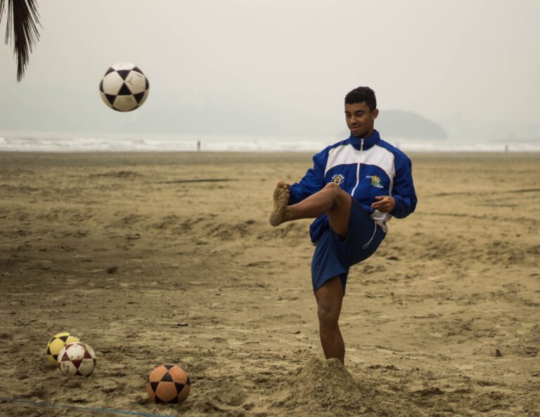 A young male athlete practices soccer on a sandy beach, showcasing skill under cloudy skies.