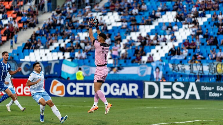 Goalkeeper successfully catches the ball during an intense football match in a stadium filled with spectators.