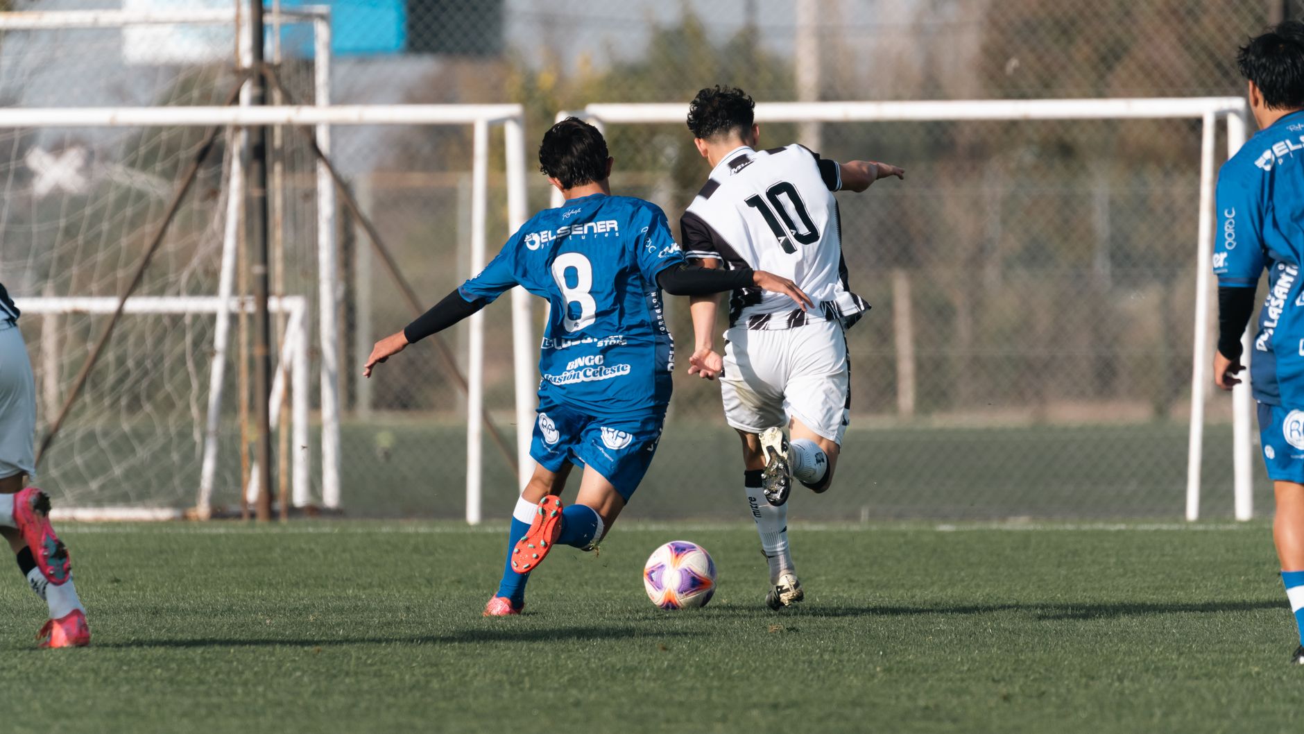 Dynamic moment in a soccer match with players competing for the ball on a clear day.