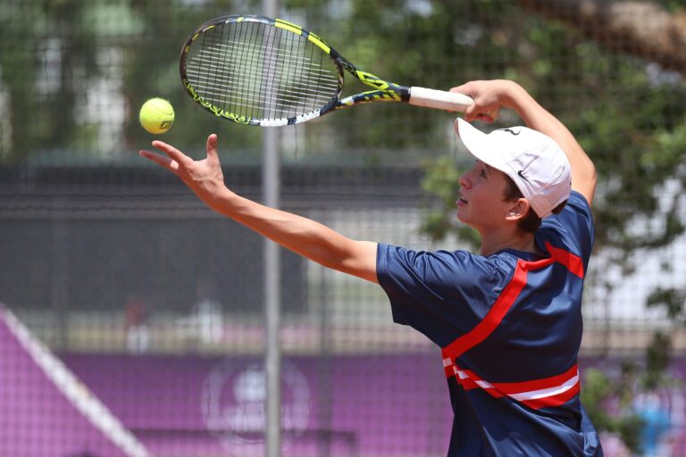 Teenage tennis player in action serving on a sunny outdoor court.