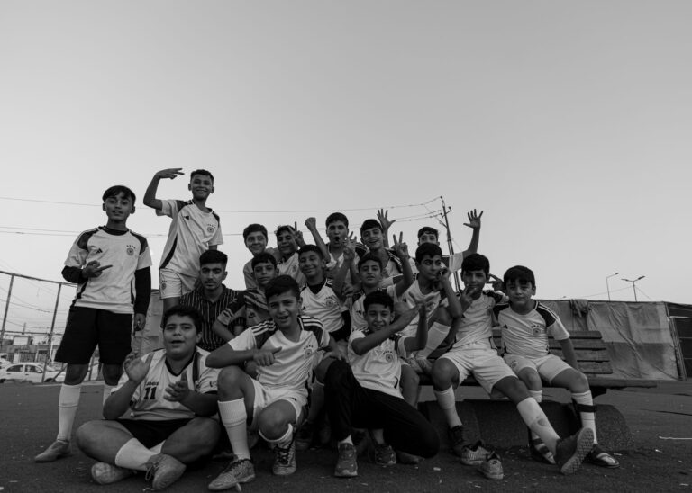 Black and white photo of young boys posing cheerfully in sports uniforms outdoors.