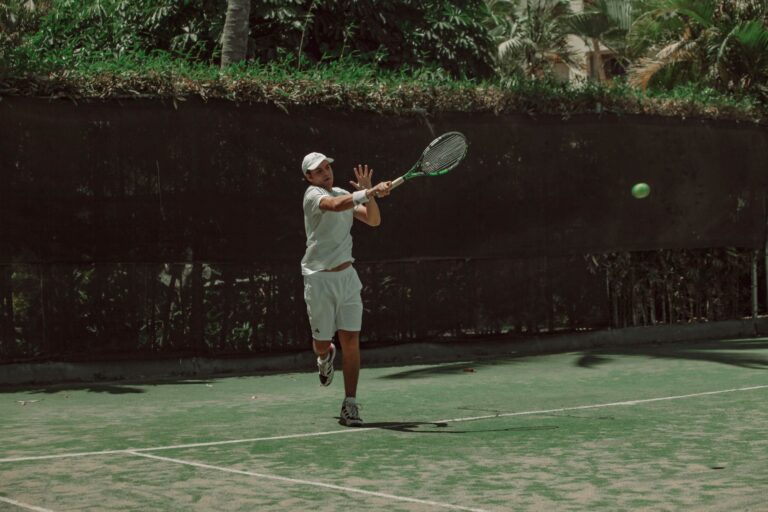 Male tennis player hitting a forehand shot on an outdoor court during a sunny day.