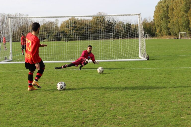 A soccer player prepares to take a shot as the goalkeeper dives to save in an outdoor match.