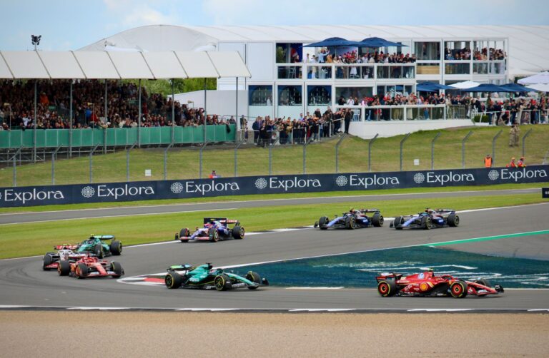 High-speed Formula 1 race at Silverstone Circuit, England, with enthusiastic spectators.