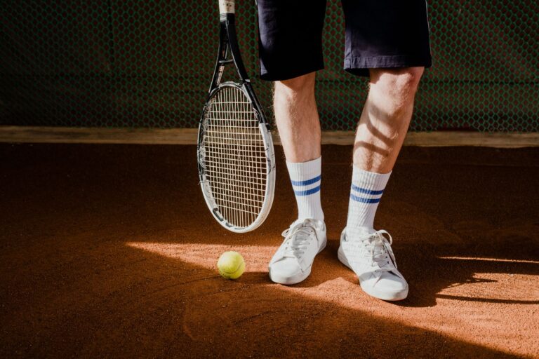 Close-up of a tennis player with racket and ball on a clay court, wearing white sneakers and socks.
