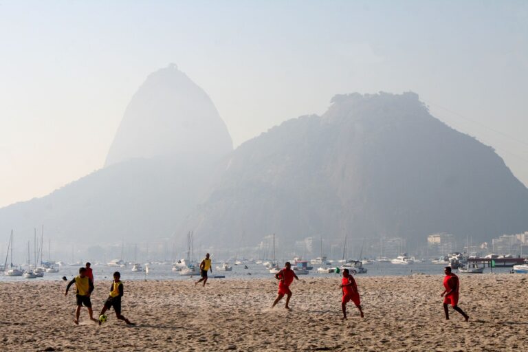 Young people playing soccer on a beach with Sugarloaf Mountain in the background.