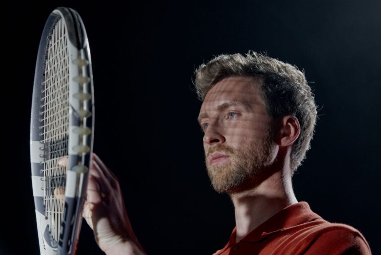 Portrait of a serious male tennis player holding a racket with a black background.