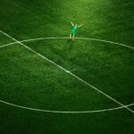 A soccer player celebrates on an empty field, spotlighted in the stadium's center circle.