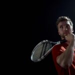 A thoughtful male tennis player holding a racket, set against a dark background.