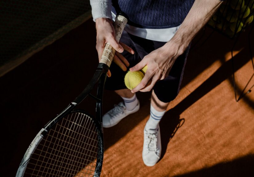 A tennis player prepares for a serve, holding a racket and tennis ball on a clay court.