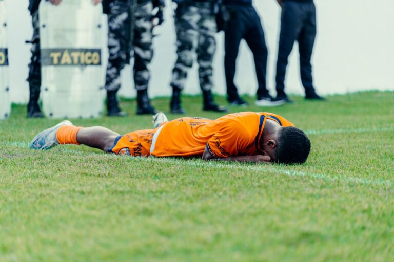 Injured football player in orange jersey lying on field with police presence.