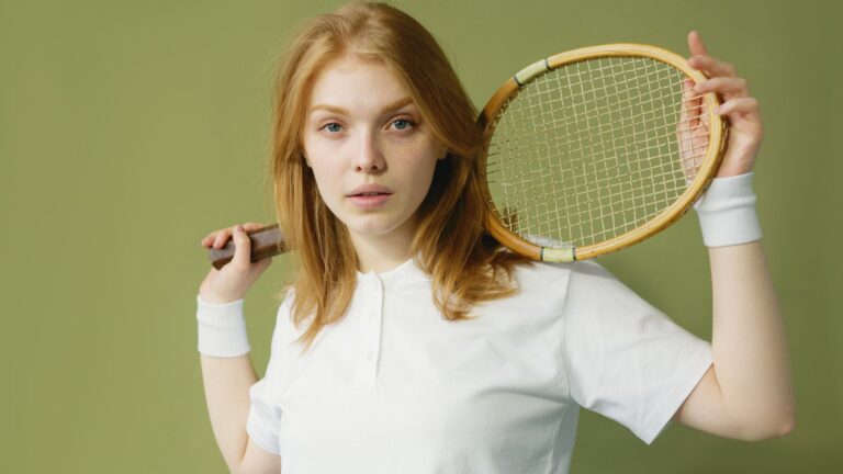 Portrait of a blonde woman with a tennis racket on her shoulder against a green background.