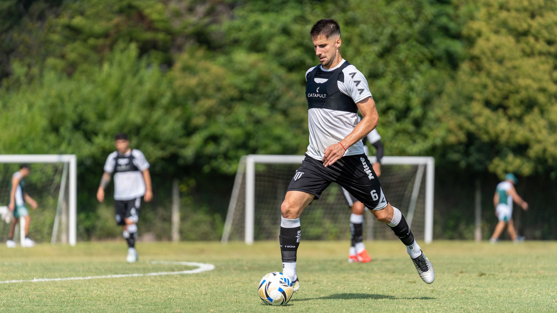 A soccer player is skillfully dribbling the ball on a sunny outdoor field during training.