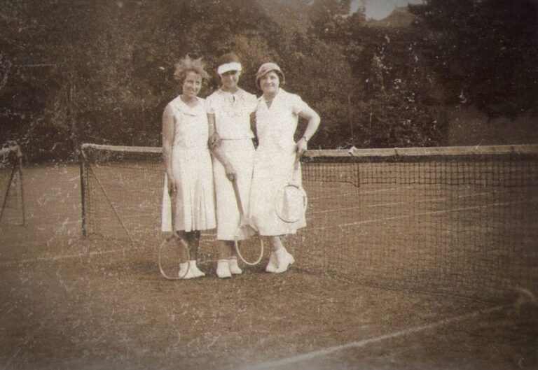 A classic vintage photo of three women on a tennis court holding rackets.