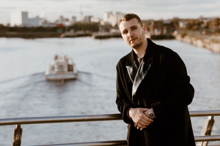 Fashionable man standing on a bridge in Manchester with the cityscape and river behind.