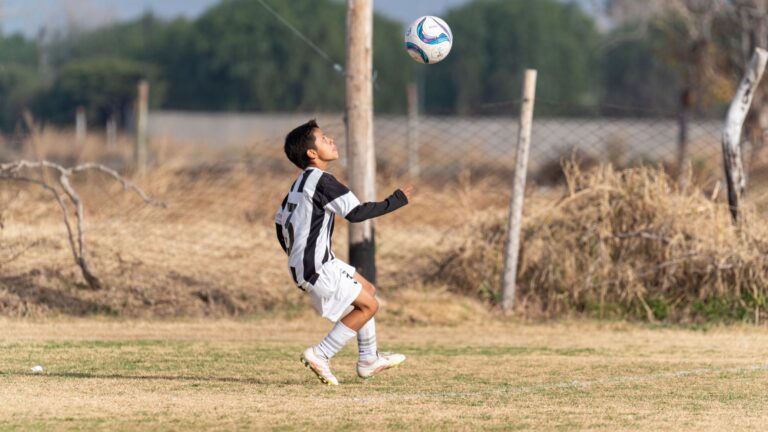 A young soccer player in action performing a header on a grassy outdoor field.