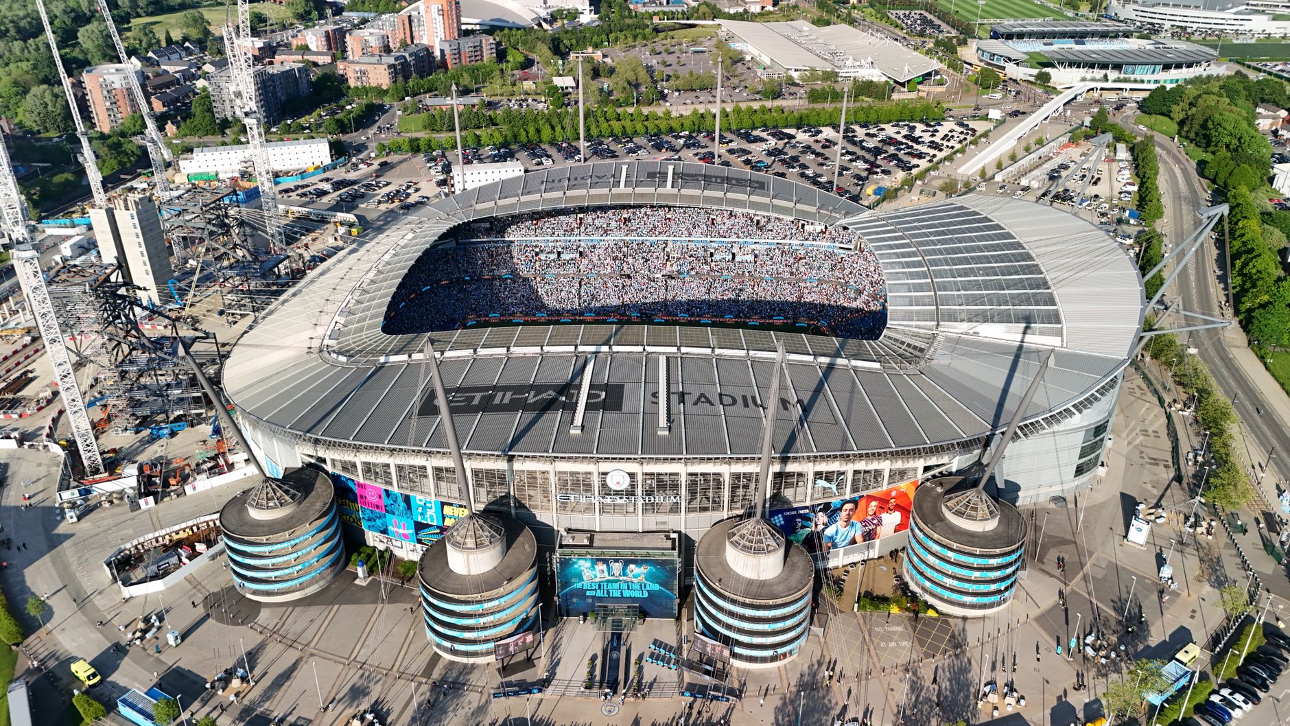 Drone shot of a packed Etihad Stadium in Manchester, England, showcasing a vibrant cityscape.