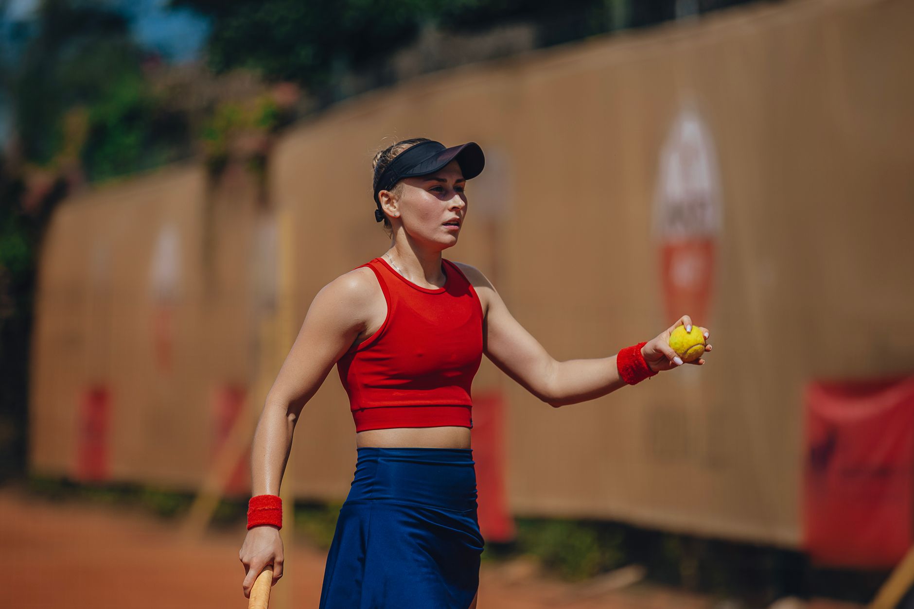 Focused female tennis player in action on an outdoor clay court during daytime.