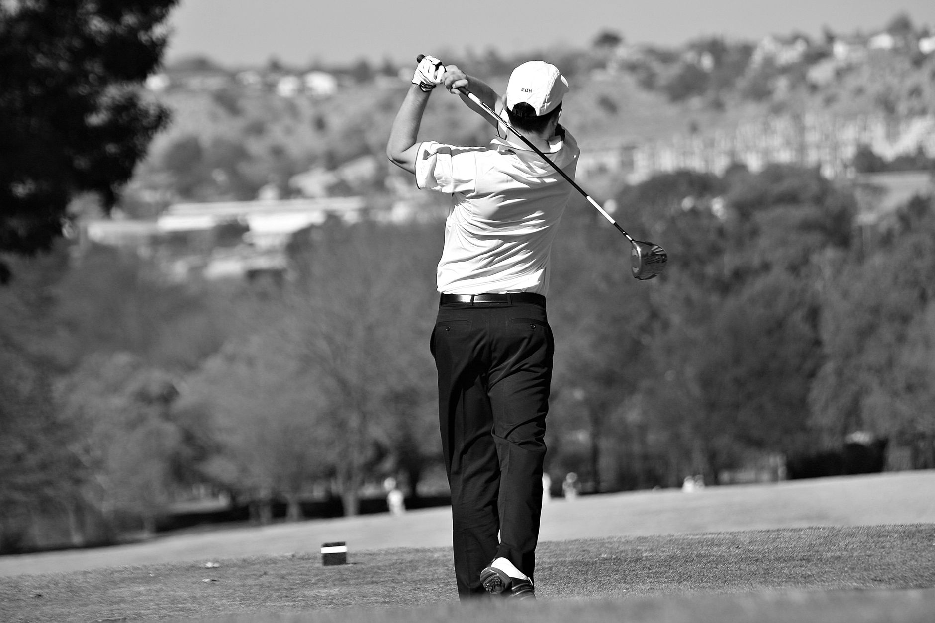 Black and white image of a male golfer swinging on a lush golf course.
