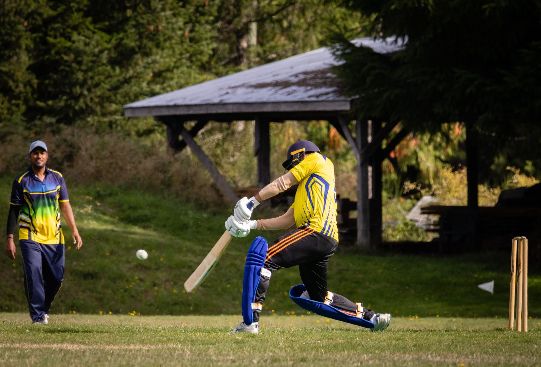 Cricketer batting an incoming ball outdoors on a sunny day.