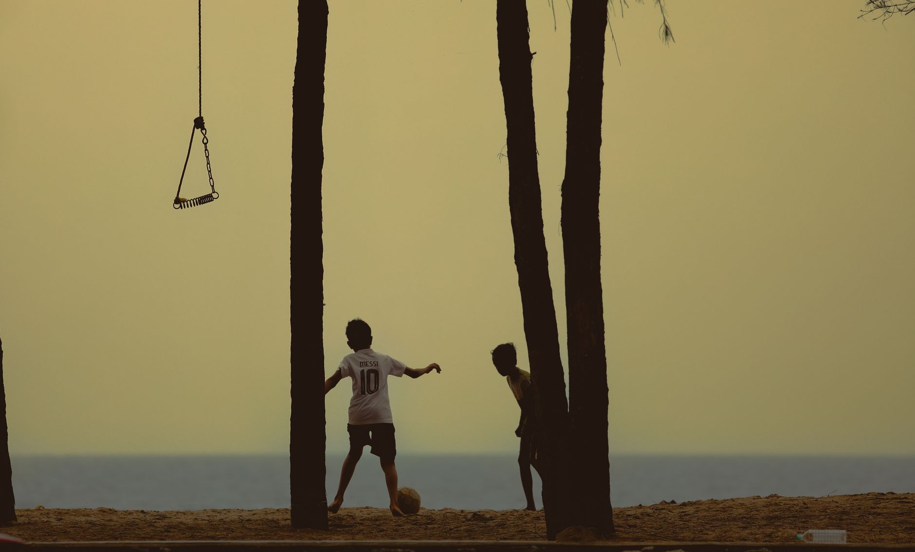 Silhouette of children playing soccer on a beach at sunset, creating a tranquil and nostalgic scene.