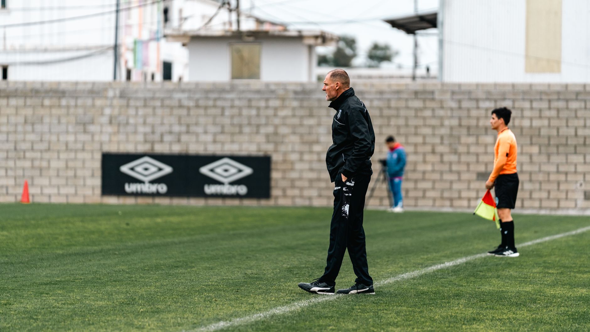 A soccer coach attentively observes a training session, standing by the sideline.