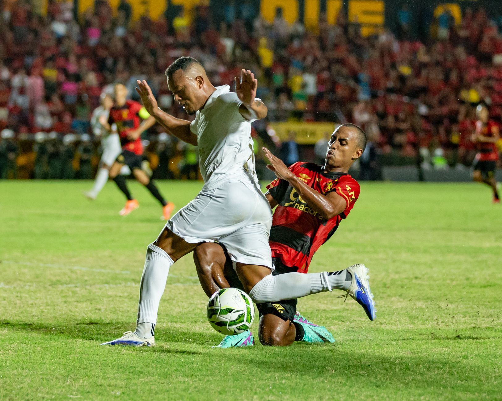 Dramatic tackle during a competitive soccer match under stadium lights.