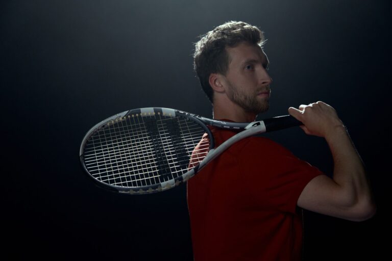 Portrait of a male athlete with a tennis racket in a dark studio setting, highlighting his profile.
