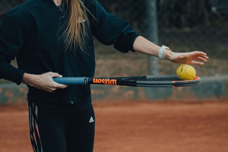 Close-up of a woman holding a tennis racket and ball ready for a serve on a clay court.