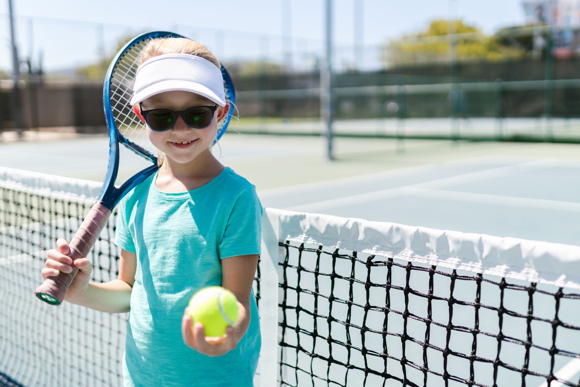 Smiling girl holding tennis racket and ball on a sunny tennis court.