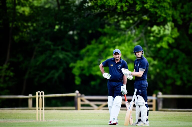 Two cricket players in gear discussing strategy on a sunny day outdoors, ready to play.