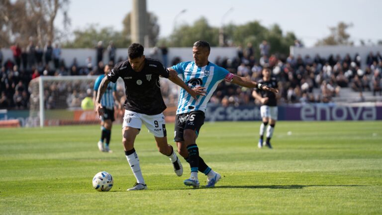 Two soccer players compete for the ball on a sunny day during a lively match.