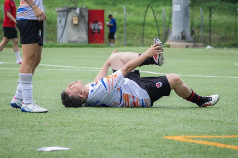 A soccer player lies on the field with an apparent leg injury during a game, needing assistance.