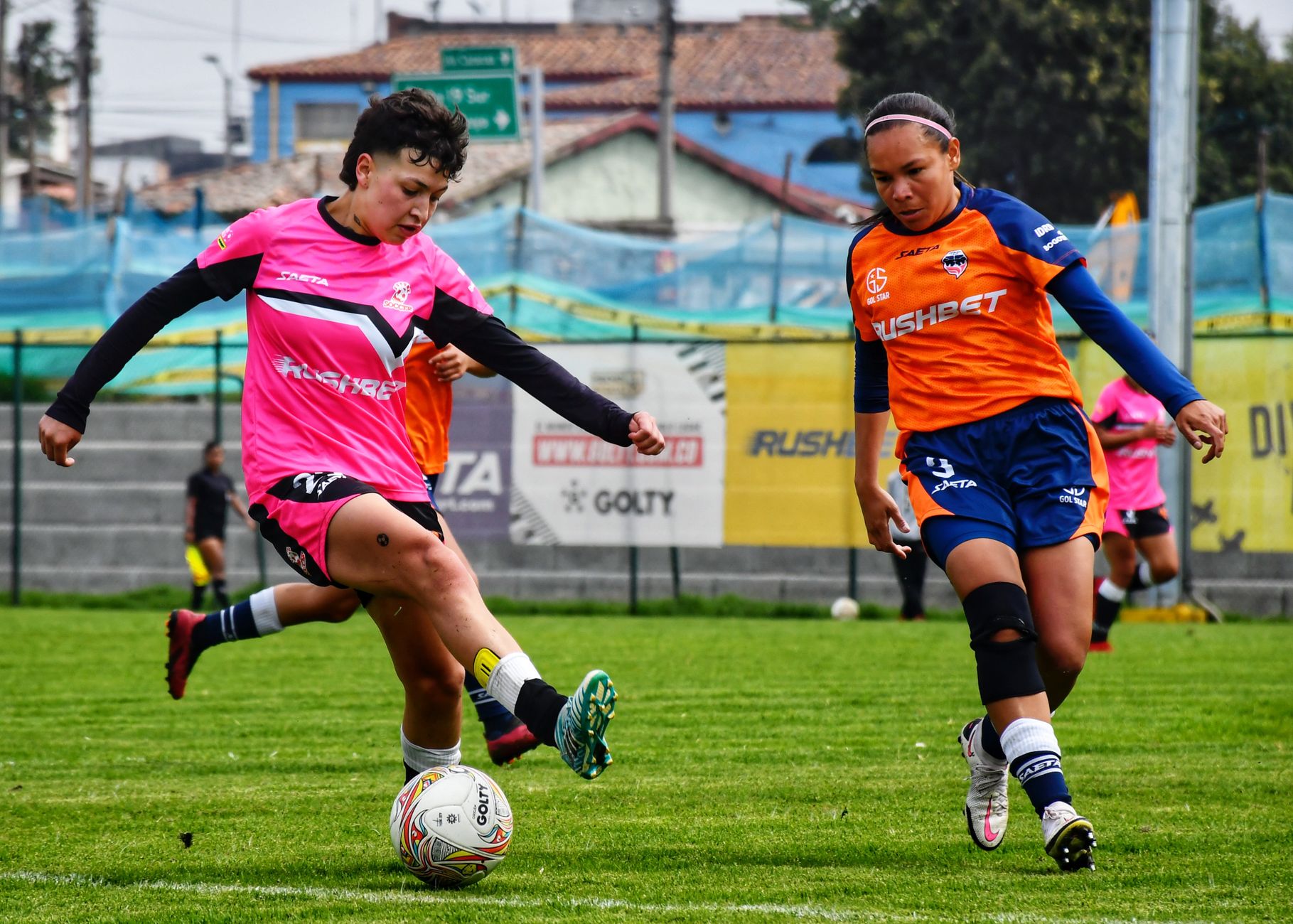 Action shot of women playing soccer in colorful uniforms on a sunny day.