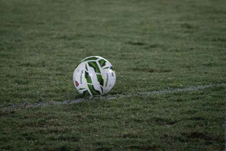 A soccer ball resting on a grass field, captured during nightfall with visible dew.