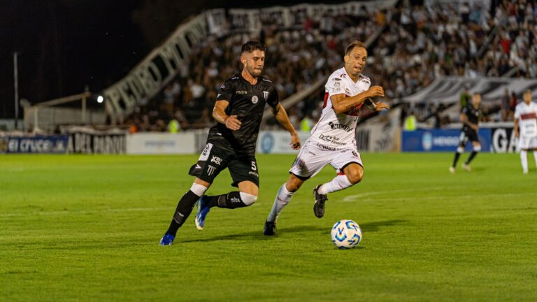 Two soccer players competing vigorously during a night match in a stadium, full crowd in background.