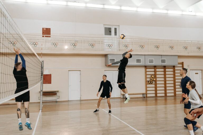 Competitive indoor volleyball match with athletes spiking the ball over the net.