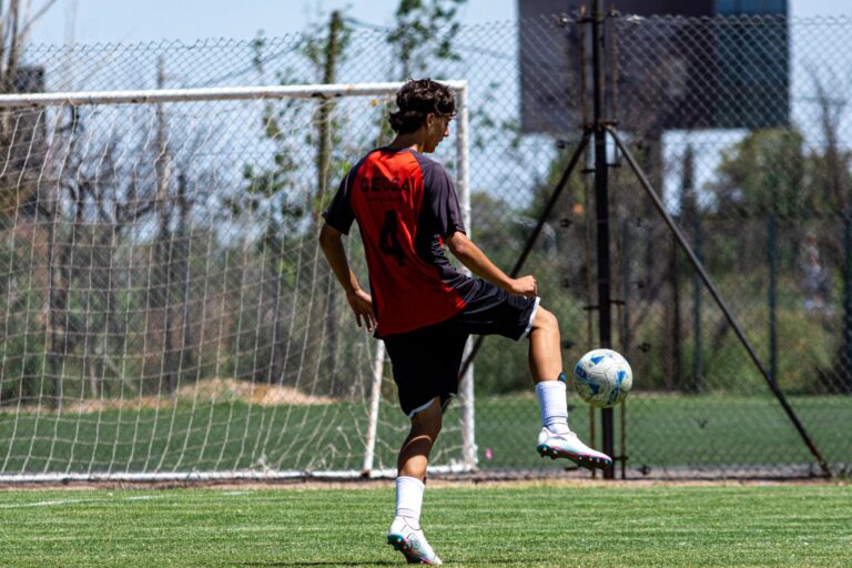 Teenager in red jersey playing soccer on an outdoor field during daytime.