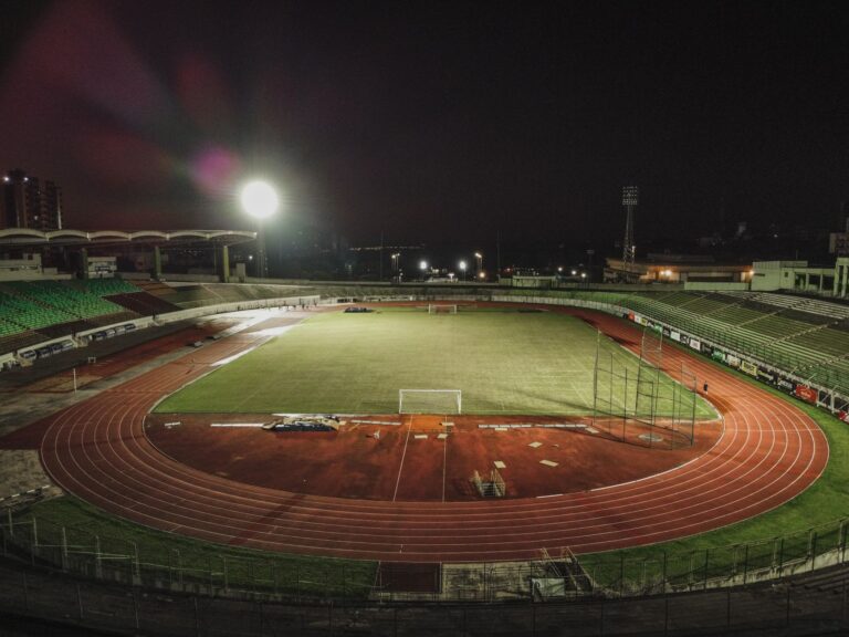 A captivating nighttime aerial view of Estádio Willie Davids in Brazil, showcasing its illuminated field and track.