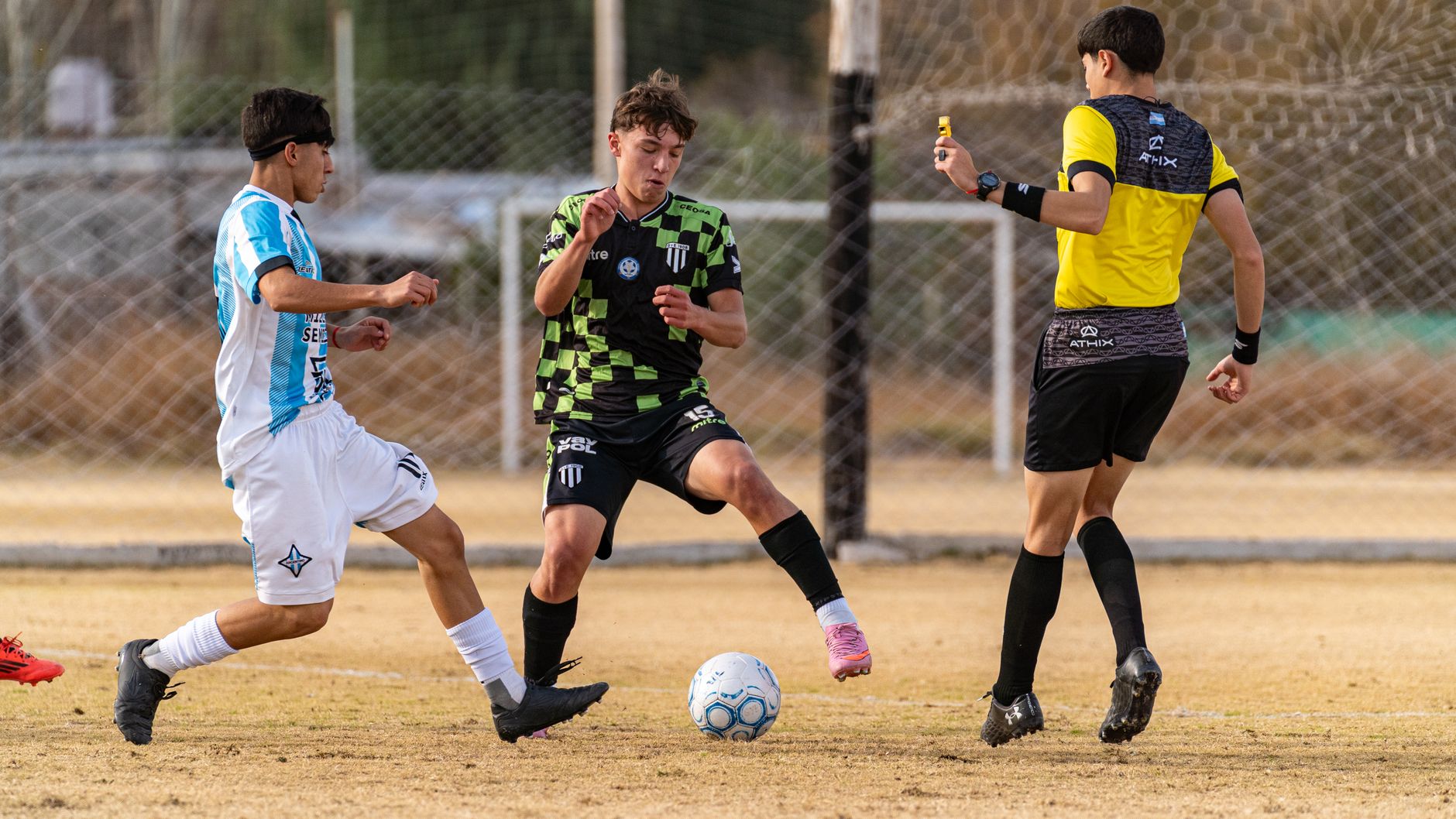Soccer players in action during a competitive match with referee interaction.