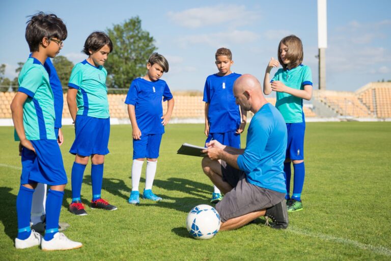 Coach guiding young soccer players on a lush green field under a clear sky.